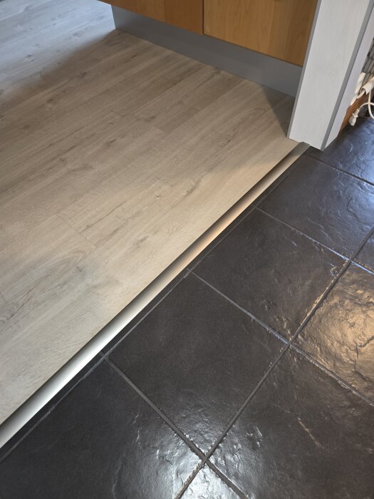 Klinkergolv med smal fog mot kökets trägolv. Fogens spruckna tillstånd syns nära kökets skåp.