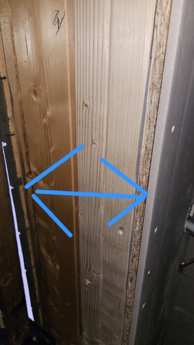 Trävägg med gipskant och blå pilar som indikerar placering av utsalning inför garageportsmontering.