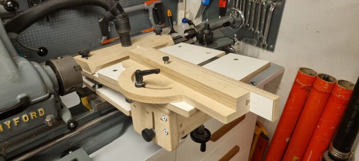 Bild av en svarv med träjigg monterad, omgiven av verktyg och maskiner i en verkstad.