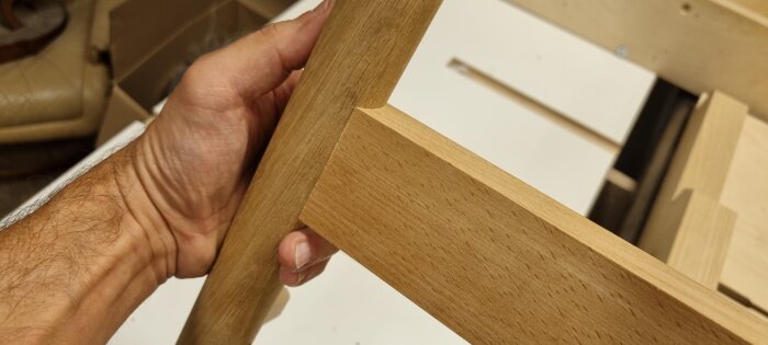 Hand som håller i fästet på en trebent träram, troligen en del av snickeriprojektet i beskrivningen.