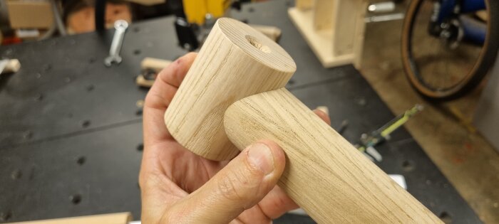 Hand håller en svarvad träcylinder med ett hål i mitten, en del av ett pågående byggprojekt.