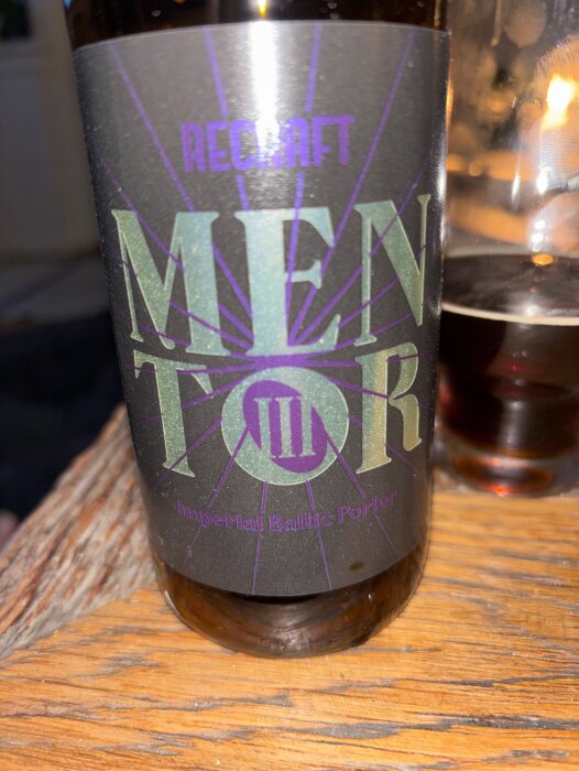 Flaska med etikett "RECRAFT MENTOR III Imperial Baltic Porter" fotograferad på ett bord med öl i glas bakom.