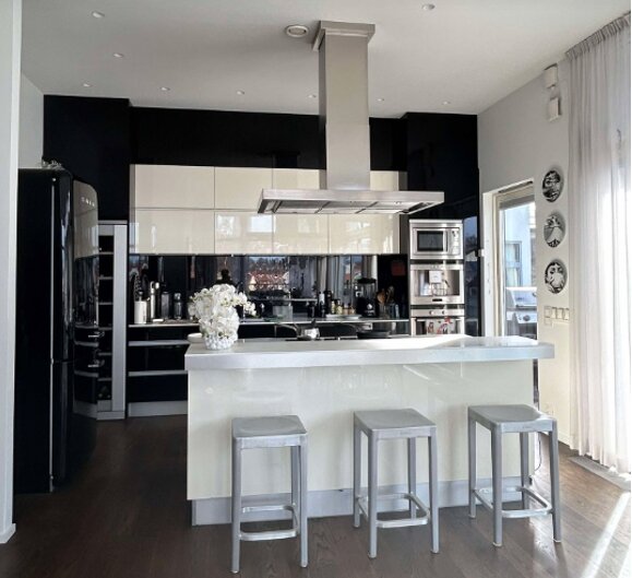 Modernt kök med köksö, tre barstolar, mörka skåp, vit köksbänk och infälld häll. Ugn och mikrovågsugn i högskåpet till höger.