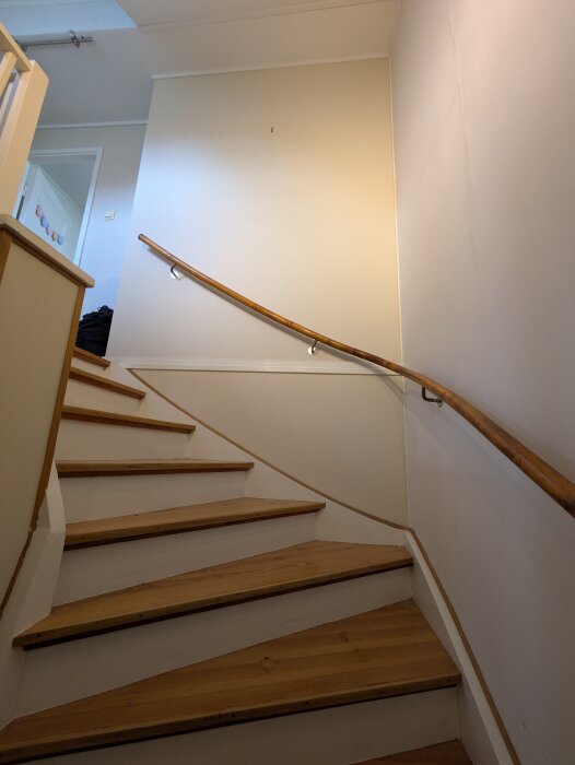 Trappa med trästeg och ljus vägg, räcke följer trappan upp. Diskuteras om bröstpanelens höjd och form; raka linjer eller följa ledstångens böjning.