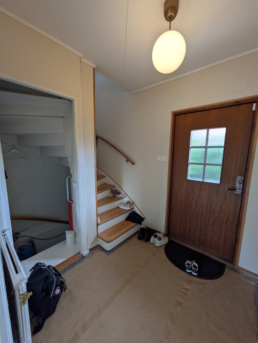 Trappa och dörr i en hall, med skor på golvet och en rund lampa i taket. Funderingar kring bröstpanelens placering i trappan.