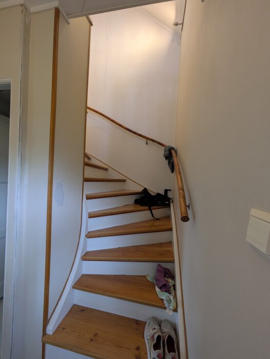 Spiraltrappa med trästeg och ledstång. Kläder och skor ligger på trappstegen. Väggar planeras för bröstpanel och tapet vid renovering.
