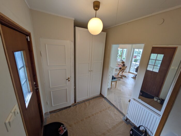 Vy över hall med vita dörrar, träpanel, spegel och lampa i taket; parkettgolv i angränsande rum syns också.