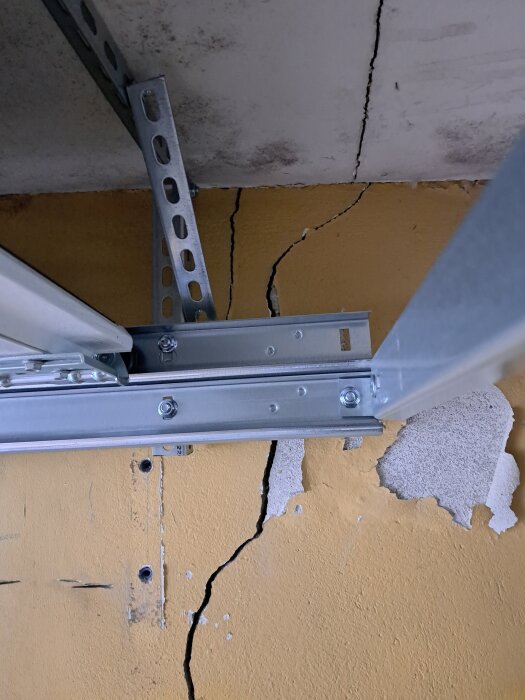 Spricka i garagevägg med gul yta bakom en metallstruktur.