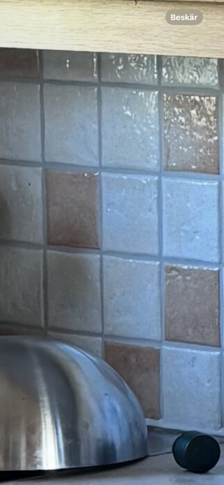 Kökskakel med ljus- och mörkbeige rutor bakom en rostfri skål och en mörkgrön kork.