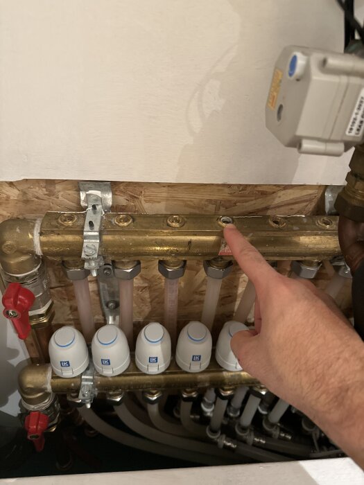 En hand pekar mot rörkopplingar på en golvvärmefördelare med flera ventiler, där slinga nummer 4 inte går att spola.