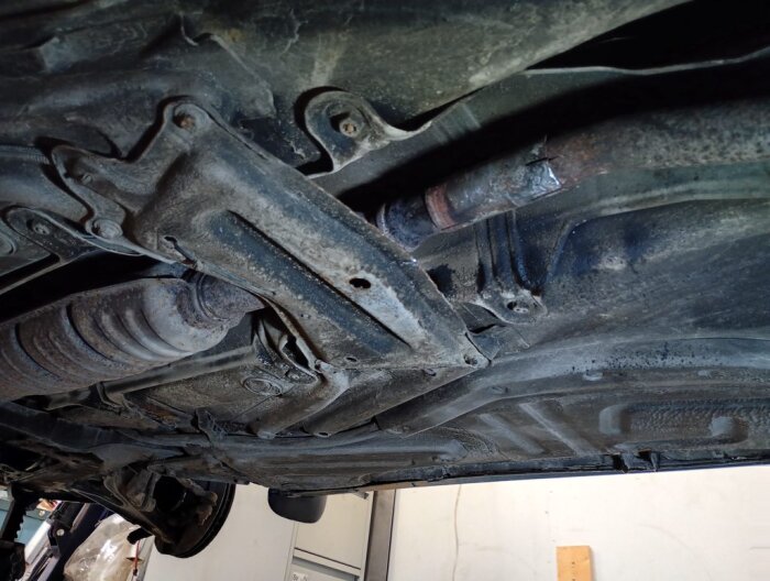 Undersida av en Volvo med ett lagat avgasrör där två rör varit på varandra. Reparation synlig mitt under bilen, rost och märkbar skarv.