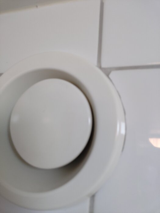 Ventilationsdon på en vit kakelvägg, med snedställd kon i mitten som kan justeras, men verkar inte sitta fast ordentligt.