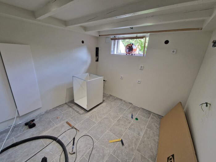 Renovering av källare med ljusgrått klinkergolv, halvmonterat skåp, verktyg och fönster med utsikt.