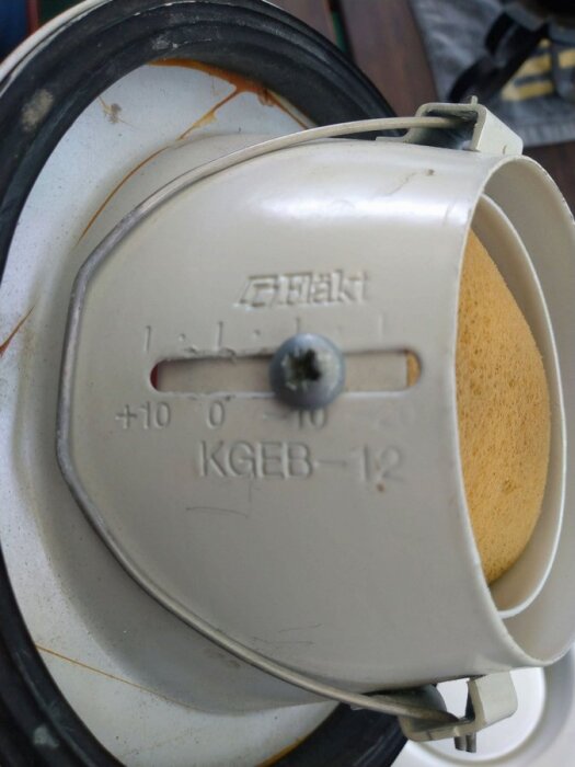 Justerbar ventilationsenhet med en skruv i mitten och texten "KGBE 12" på framsidan, skruven är inte helt åtdragen.