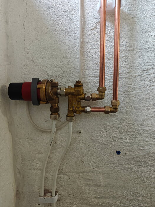 Rör och kopplingar på vägg, kopplade till en vattenpump i ett rum med vitputsad yta.