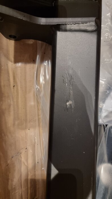 Dragkroksdel med skadad lack och repor, liggande på plast och trä i ett garage.