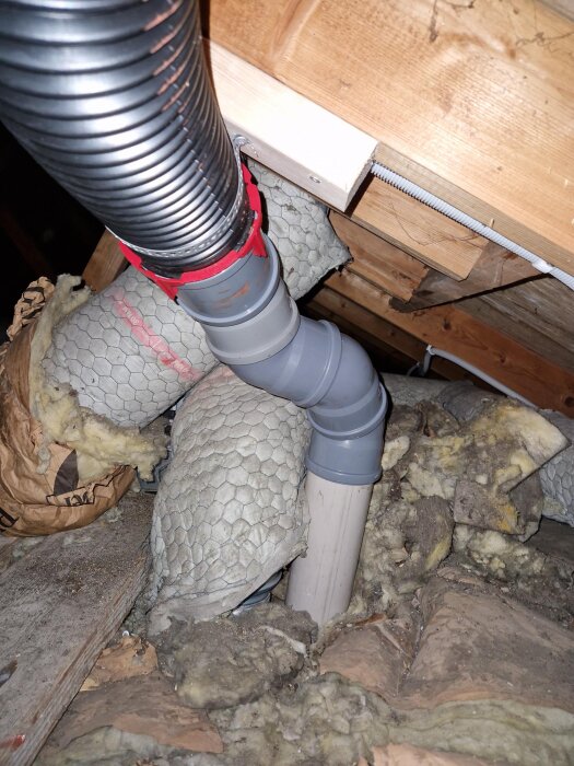 Ventilationsslang med extra regel mellan takstolar på vinden, omgiven av isolering och byggmaterial.