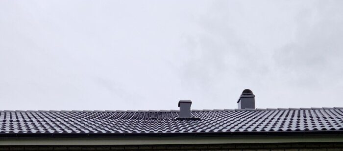 Tegeltak med två skorstenar under en molnig himmel.