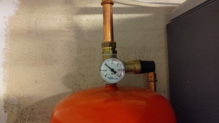 Expansionskärl med kopparrör och manometer som mäter trycket i värmesystemet, monterat på en vägg.