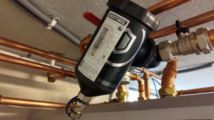 Magnetfilter från Sentinel anslutet till kopparrör och rördelar i ett rörsystem, set underifrån.
