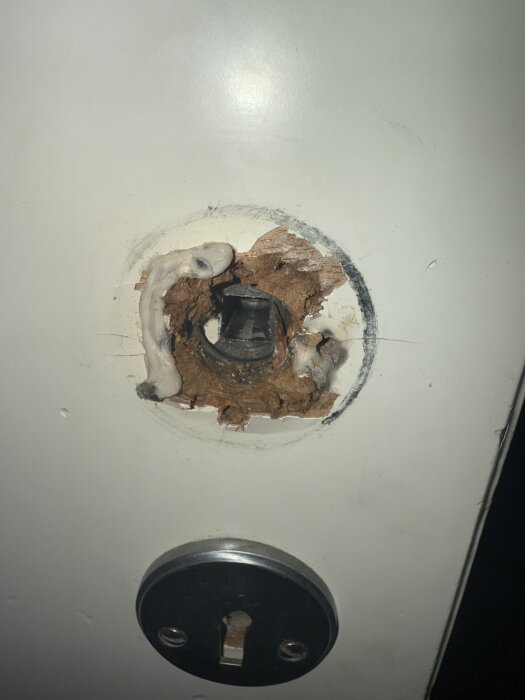 Uppriven dörryta där träflisor syns runt ett dörrhandtag. Dörrhålet är lagat med någon form av spackel.