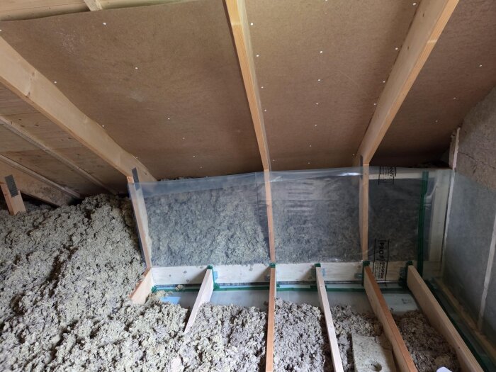 Isoleringsarbete på övervåning i ett 1,5 planshus med lösull och plastfolie, synliga träbalkar och skivor, fokus på lufttäthet och ångspärr.