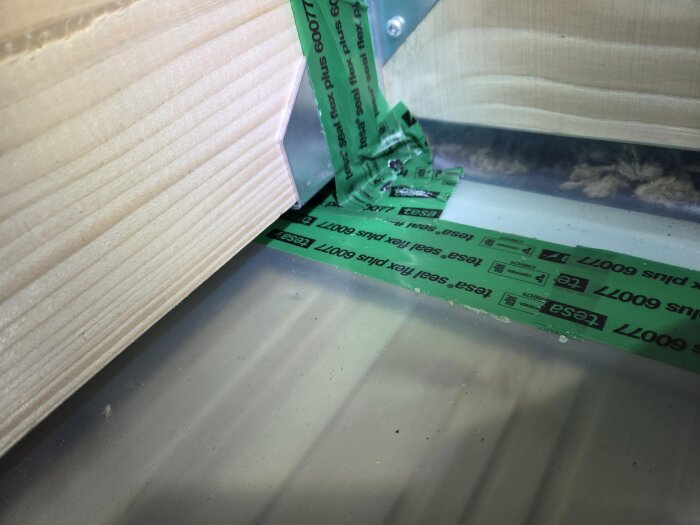 Närbild på konstruktion med träbalk, metallbeslag och ångspärr, där grönt tejp används för tätning vid skarv.