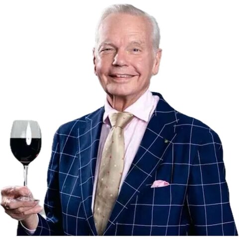 En man i kostym håller ett vinglas och ler.