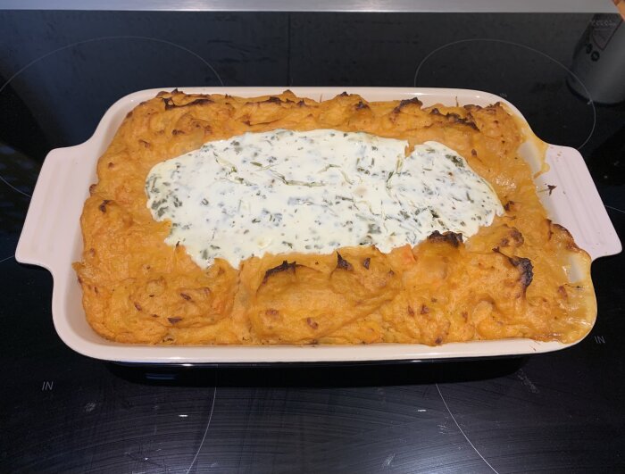 Fiskgratäng med alaskan pollock toppad med sötpotatismos och krämig sås i en ugnsform på spishällen.