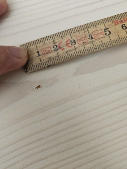 Mätsticka mot ljus träyta med liten repa.