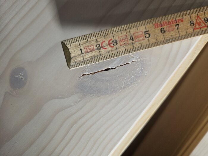 Måttstock bredvid en spricka i en träyta.