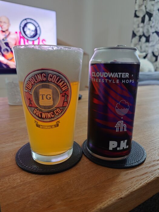Glas med öl från Toppling Goliath Brewing Co. och en Cloudwater-burk på ett bord framför en tv.