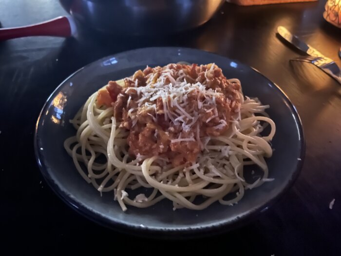 Spaghetti med salsicciafärs, toppad med riven ost, serverad på en grå tallrik.
