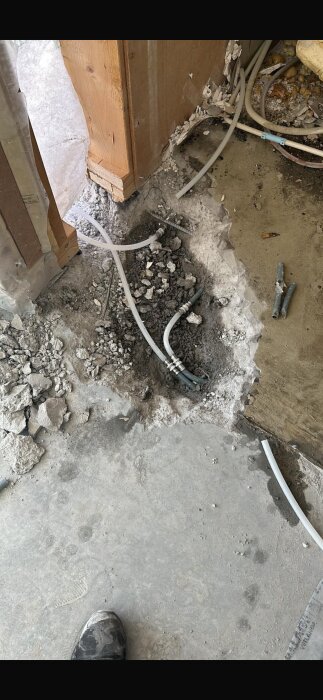 Rivning av vägg med exponerad rördragning och spillror på betonggolv.