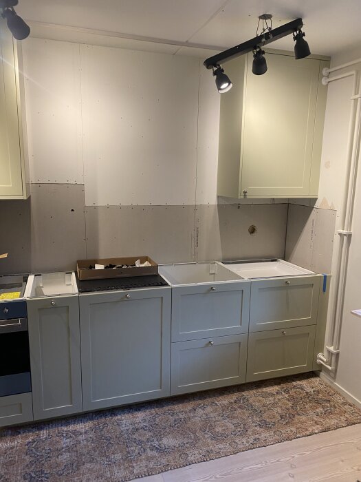 Kök med gröna skåp, oavslutad vägg redo för spackling; fråga om behov av extra skiva inför målning.