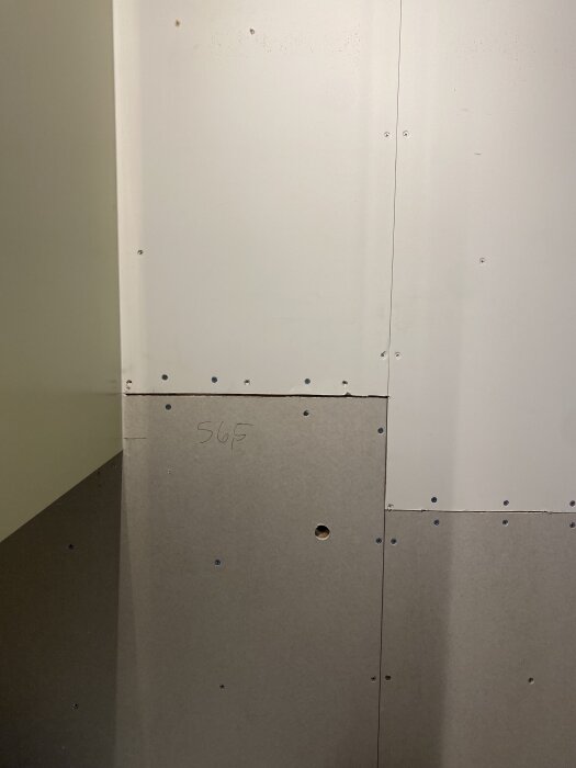 Vägg med gipsskivor och skruvar, några synliga hål och siffran "565" skriven på en skiva.