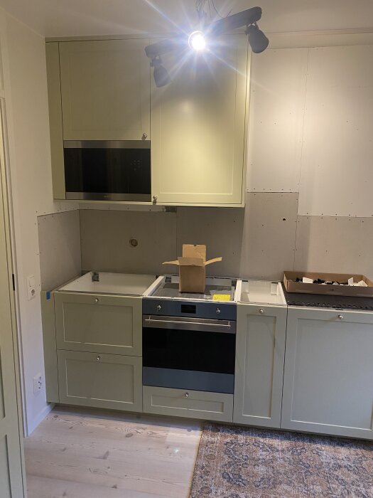 Kök med halvfärdig installation, vägg bakom i rå gipsskiva, målning och spackling diskuteras.