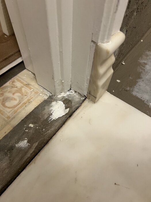 Skadad tröskel i byggprojekt, med synliga lappar av tätskikt och vattenfläckar på golvet. Avslutningen vid tröskeln ser ojämn ut.