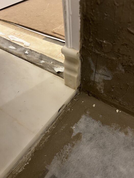 Närbild på tröskel och golv med oregelbundet avslut, delvis blött tätskikt och skarv.