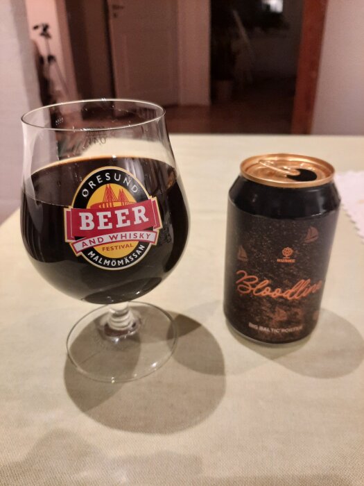 Ett glas med mörk öl från Malmömässans öl- och whiskyfestival bredvid en burk "Bloodline Big Baltic Porter" på ett bord.