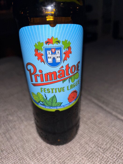 Flaska Primátor Festive Lager med blå etikett och färgstarkt emblem, en öl med sötma som passar till mat.
