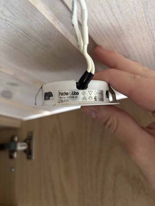 Hand som håller en halogenspott med synliga kablar, monterad under ett skåp.