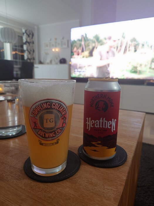 Ölburk med Northern Monk Heathen IPA och ett glas öl på ett bord framför en TV.