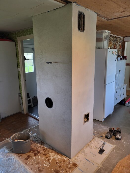 Vitmålad skorsten med sotlucka, ventilationslucka och kaminadapter. Verktyg och skyddspapper ligger på golvet runtom.