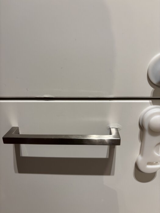 Skåplucka med svullnad och avskrapad färg, metallhandtag och en plastdetalj till höger.