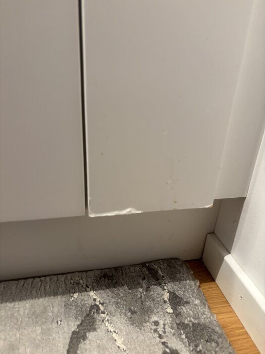 Svullna träskåp med avskavd färg vid golvet, visar slitaget på ytan.