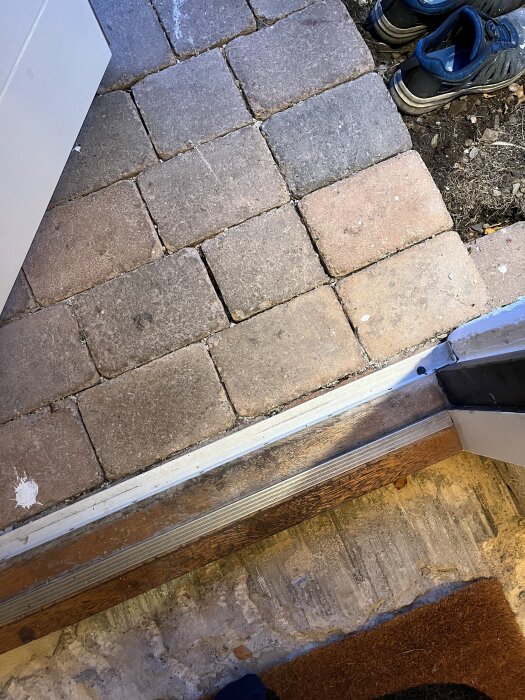 Tröskelområde med stenar på ingången som ska bytas, några skor syns vid sidan.