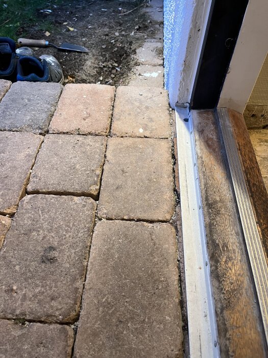 Ytterdörrens tröskel med närliggande stenläggning som ska bytas ut; även en spade och skor syns vid sidan.