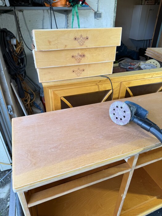 Ett vitrinskåp under renovering, visar avtagna lådor och en slipmaskin på en yta som håller på att slipas.