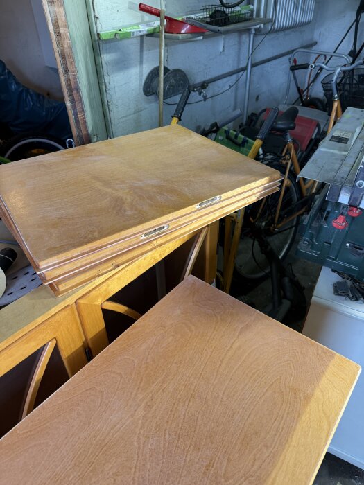 Vitrinskåpsdörrar och lådor under renovering, placerade i ett verkstadsutrymme med cyklar och verktyg i bakgrunden.